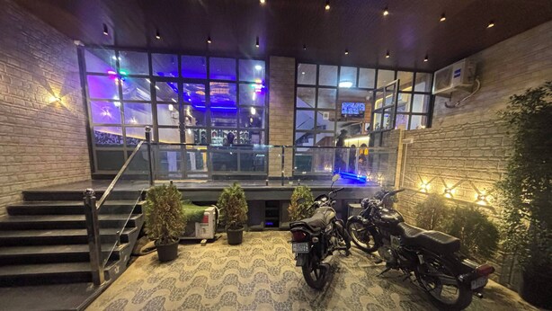 Un vaste espace intérieur doté d’un escalier menant à un balcon, agrémenté de plantes en pot et où sont stationnées des motos sur un sol à motifs.