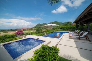 Una piscina con sillones de descanso y una pérgola, rodeada de vegetación y vistas a las colinas.