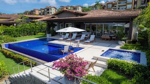A swimming pool with lounge chairs and a hot tub, surrounded by lush greenery and a patio area.