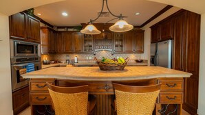 A kitchen with wooden cabinets, a large island, and two wicker chairs. - Montebello 1E 3 bdr Ocean View in Los Suenos (Jacó)