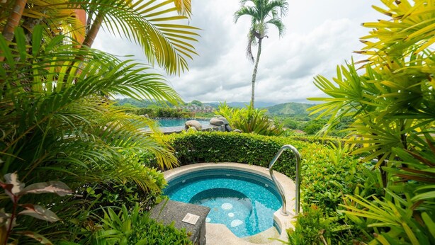 A hot tub surrounded by lush greenery and a view of a mountainous landscape. - Montebello 2E 3 bdr Ocean View in Los Suenos (Jacó)