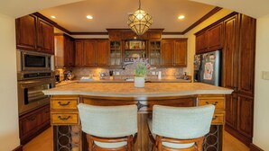 A kitchen with wooden cabinets, a large island with bar stools, a hanging light fixture, and stainless steel appliances. - Montebello 4E 3 bdr Pool View in Los Suenos (Jacó)