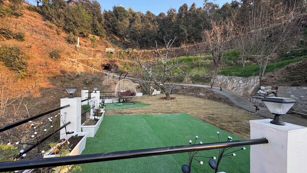 A landscaped garden with a green artificial turf area, a stone wall, and a hanging chair. - Pahadi Pind Homestay 2BR Mukteshwar - Mountain View (Mukteshwar)