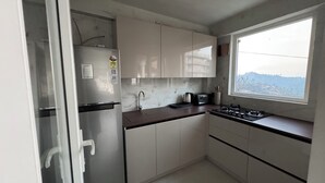 A compact kitchen with a refrigerator, stove, sink, and window. - Pahadi Pind Homestay 2BR Mukteshwar - Mountain View (Mukteshwar)
