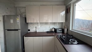 Eine kompakte Küche mit Kühlschrank, Herd, Toaster und einem Fenster mit Außenblick.
