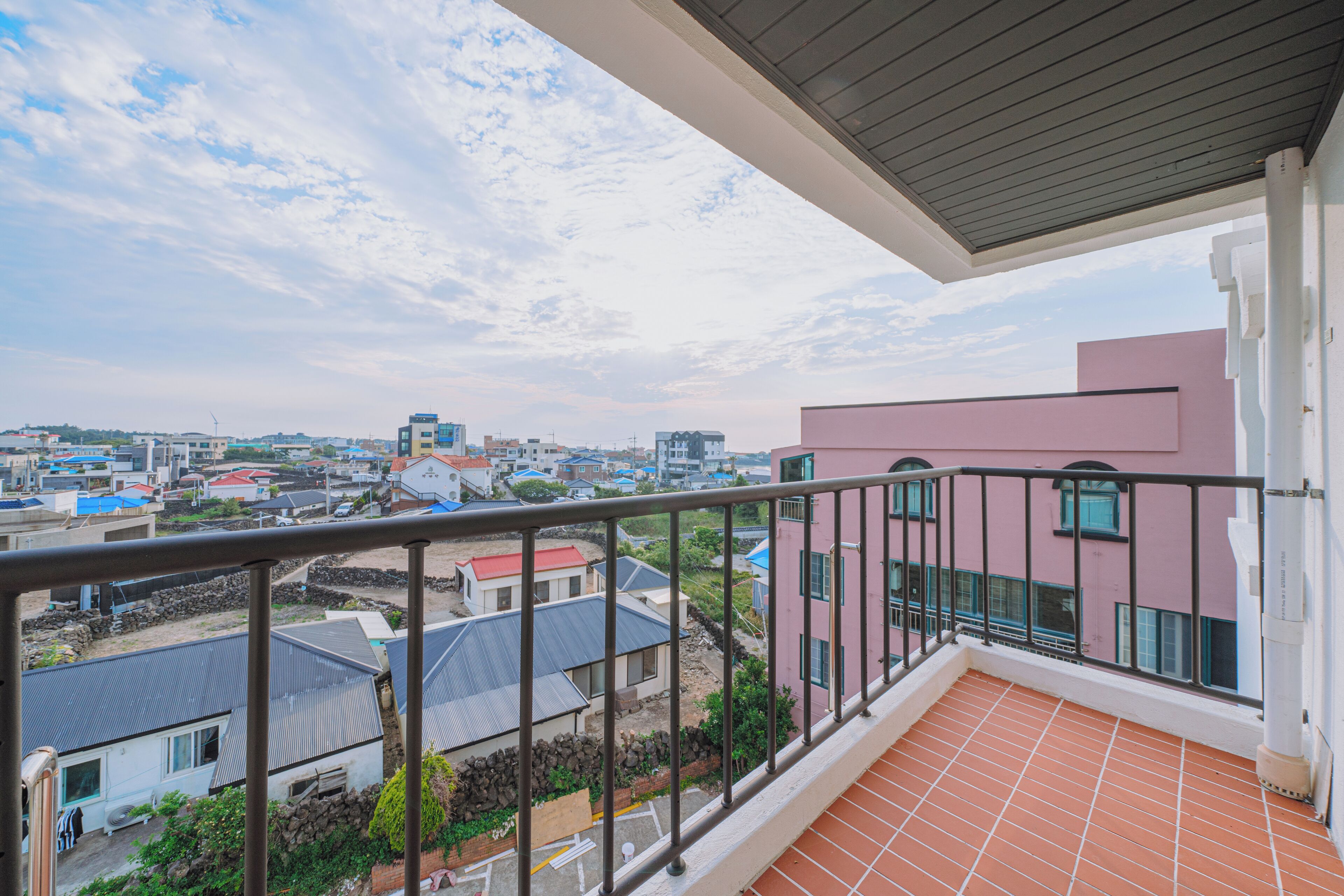 Ein Balkon mit Blick auf eine Wohngegend, einschließlich Häuser und ein pinkfarbenes Gebäude.