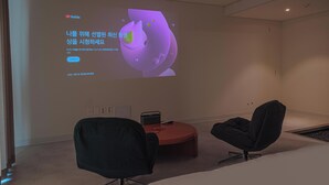 A modern room with a large screen displaying a presentation, two black chairs, a red ottoman, and a small table with a speaker. - Geumneung inn (Jeju City)