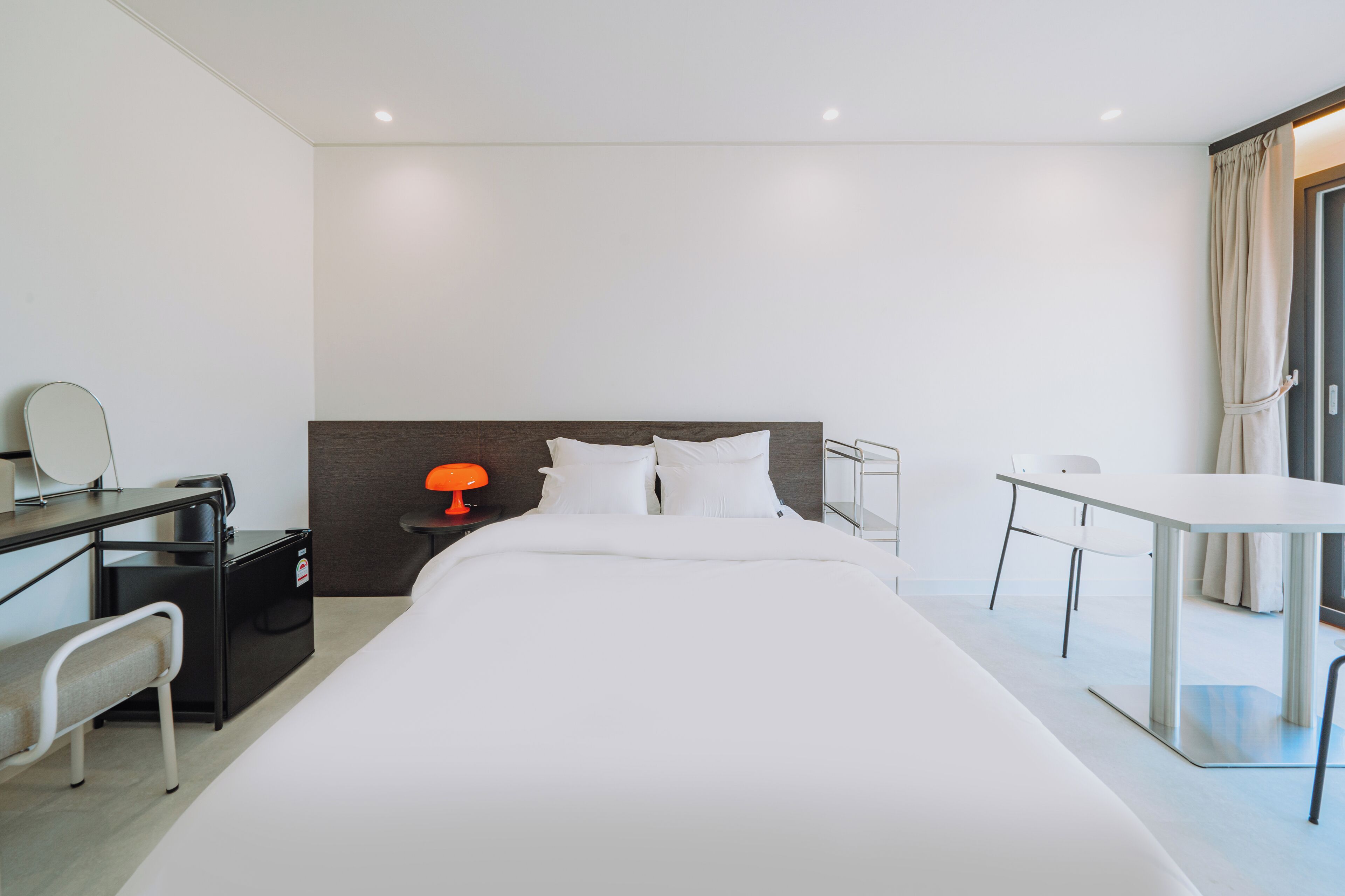 Une chambre d’hôtel avec un grand lit, un bureau avec une chaise, une petite table et une table de chevet avec une lampe.