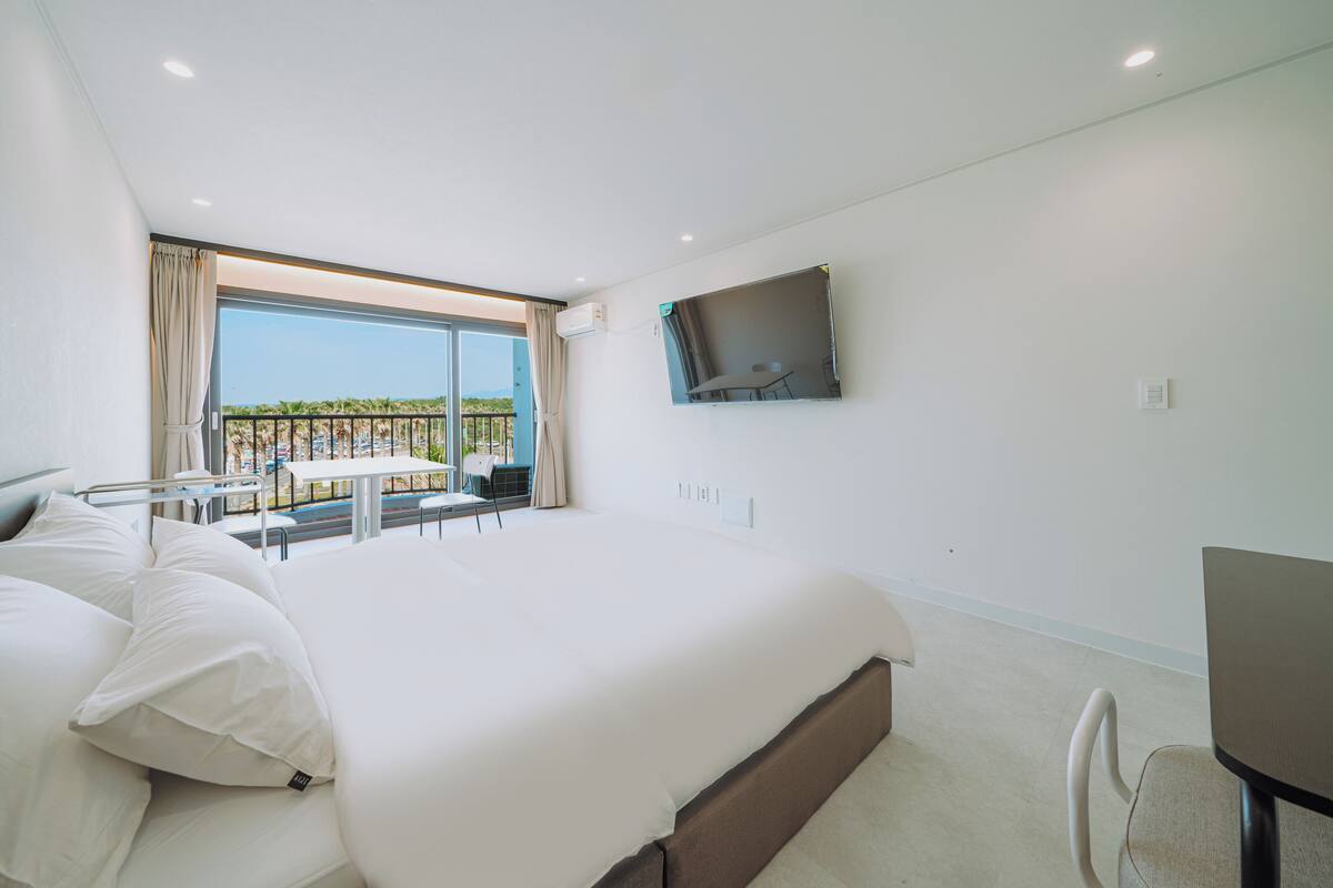 Ein modernes Hotelzimmer mit einem großen Bett, einem an der Wand befestigten Fernseher und einem Balkon mit Sitzgelegenheit.