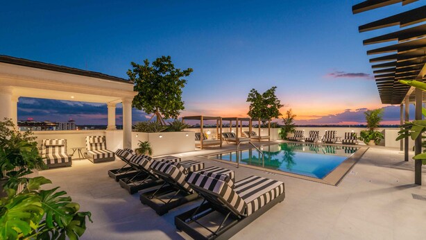 Zona de piscina en la azotea con sillones de descanso, piscina y vista del horizonte urbano al atardecer.