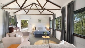 Een ruime kamer met een groot bed, een bank en een kleine tafel. Er is een raam met gordijnen en uitzicht op bomen.