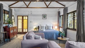 Een gezellige kamer met een bed, een bank, een klein tafeltje en een kast. Er is een raam met gordijnen en een deur met een ruit met motief.
