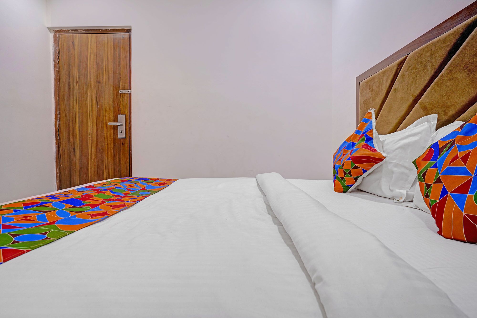 A bedroom with a bed, a wooden door, and a colorful bedspread.