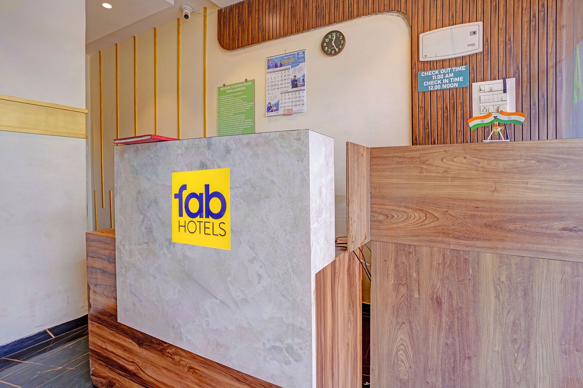 A reception desk with a 'fab hotels' logo, a wall clock, and a 'check out time' sign.