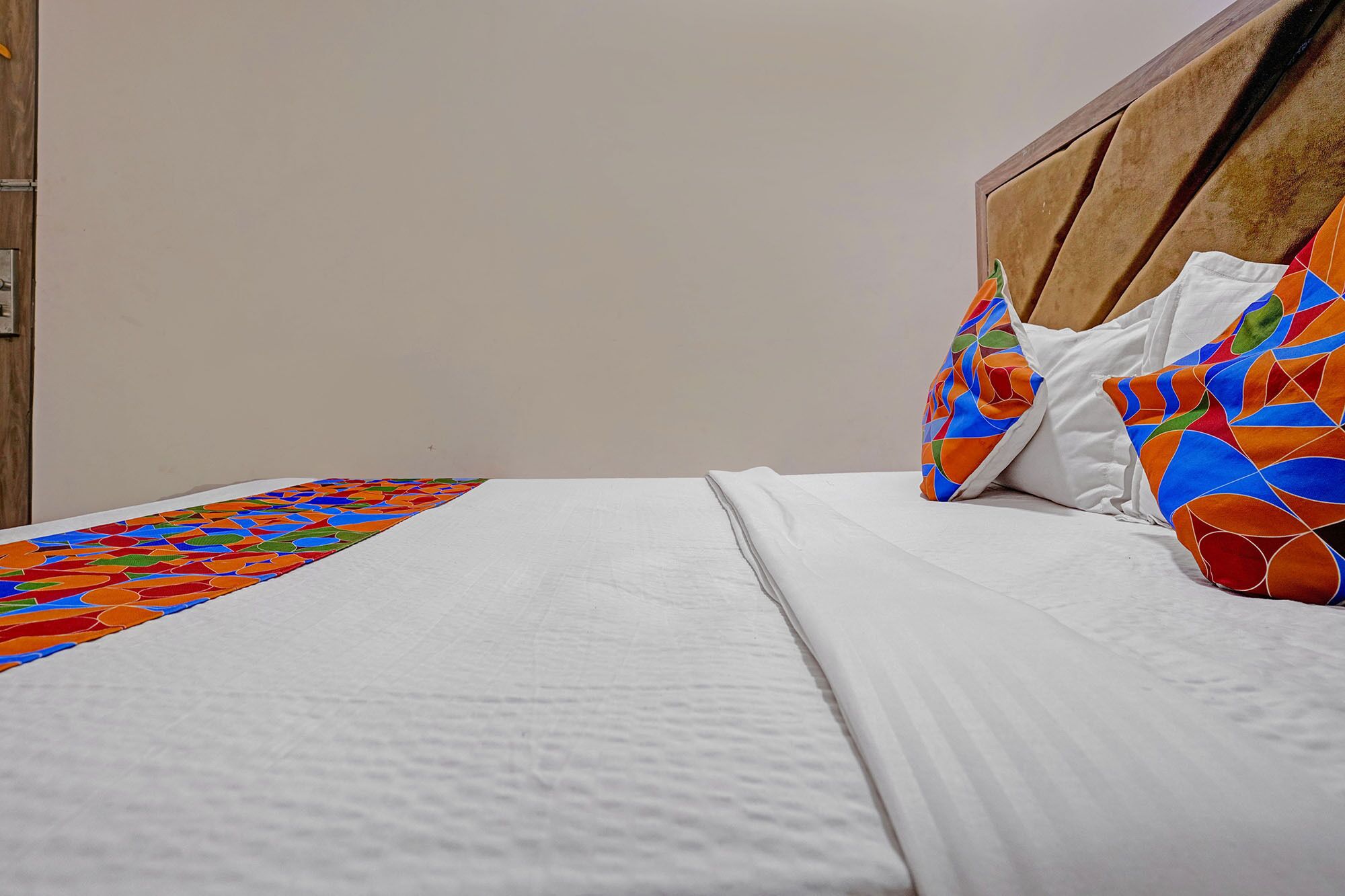 Un letto rifatto con lenzuola bianche, una coperta colorata e due cuscini con motivo geometrico.