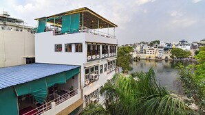 A multi-story building with balconies overlooking a river, featuring a flat roof and a covered outdoor seating area. - Fabhotel Boutique Stays Lake Pichola (Udaipur)