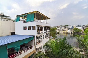 A multi-story building with balconies overlooking a river, featuring a flat roof and a covered outdoor seating area. - Fabhotel Boutique Stays Lake Pichola (Udaipur)