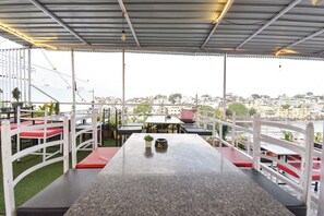 An outdoor seating area with tables and chairs, a view of a cityscape, and a metal roof structure. - Fabhotel Boutique Stays Lake Pichola (Udaipur)