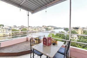 A balcony with a view of a river and cityscape, a table with a red box, and a potted plant. - Fabhotel Boutique Stays Lake Pichola (Udaipur)