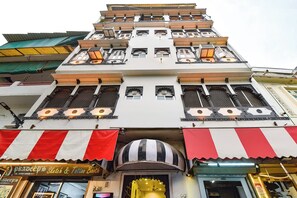 Un immeuble à plusieurs étages, avec un magasin au rez-de-chaussée, des balcons et des grilles décoratives aux fenêtres.
