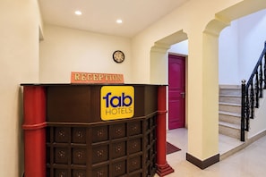 Eine Rezeption mit einem Schild für 'fab hotels', einer Uhr und einer Treppe mit einer roten Tür im Hintergrund.