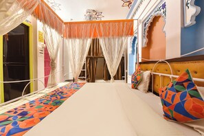 A bed with a colorful geometric-patterned runner, a tufted headboard, and a canopy with wavy drapes. - Fabhotel Boutique Stays Lake Pichola (Udaipur)