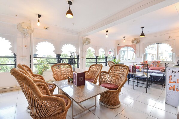 A room with wicker furniture, a table, and a balcony with a view. - Fabhotel Boutique Stays Lake Pichola (Udaipur)