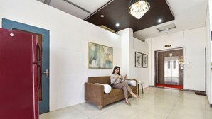 Een hotellobby met een rode deur, een bruine bank, een kroonluchter en een ingelijst schilderij aan de muur.