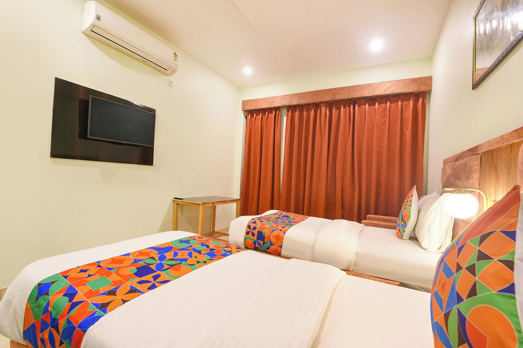 A hotel room with two beds, a TV, an air conditioner, and a window with curtains.