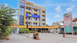 A multi-story hotel with a prominent 'Tab Hotels' sign, a parking area, and a signboard listing amenities like family restaurant, vegetarian and non-vegetarian options, and lodging services. - Fabhotel Raj (Bhor)