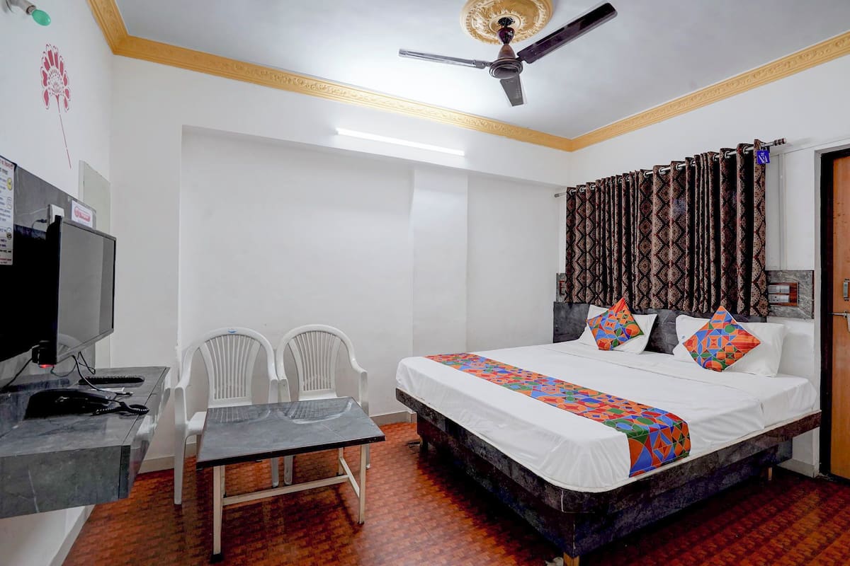 Ein Hotelzimmer mit Bett, Schreibtisch, Stühlen, Deckenventilator und gemusterten Vorhängen.