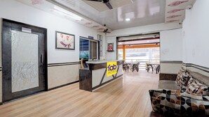 A hotel reception area with a reception desk, a seating area with a patterned sofa, and a ceiling fan. - Fabhotel Raj (Bhor)