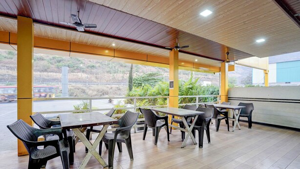 An outdoor cafe with tables and chairs, wooden flooring, and a view of greenery and a road. - Fabhotel Raj (Bhor)