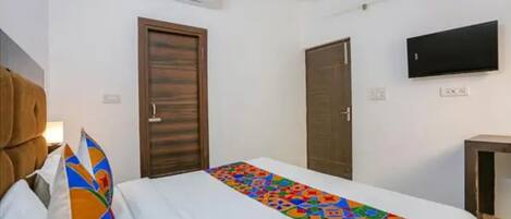 A hotel room with a bed, a ceiling fan, an air conditioning unit, a TV mounted on the wall, and two doors.