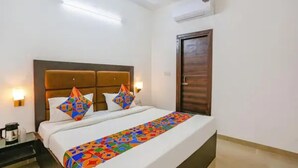 Una habitación de hotel con una cama grande, cabecera de madera, dos lámparas de pared, una puerta de madera y una mesita con cafetera.