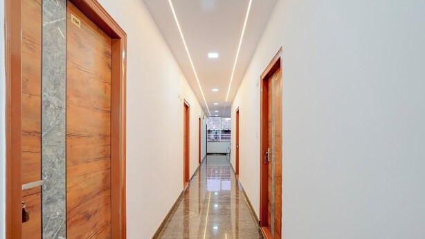 A hotel hallway with wooden doors, a marble floor, and recessed lighting. - Via Guru Residency - Kengeri (Bangalore)