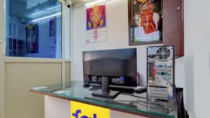 A hotel reception desk with a computer monitor, a keyboard, and a server rack. There is a calendar on the wall and a sign that reads "fab hotels". - Via Guru Residency - Kengeri (Bangalore)