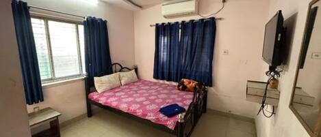 A bedroom with a bed, a ceiling fan, an air conditioner, a TV, and a window with curtains.