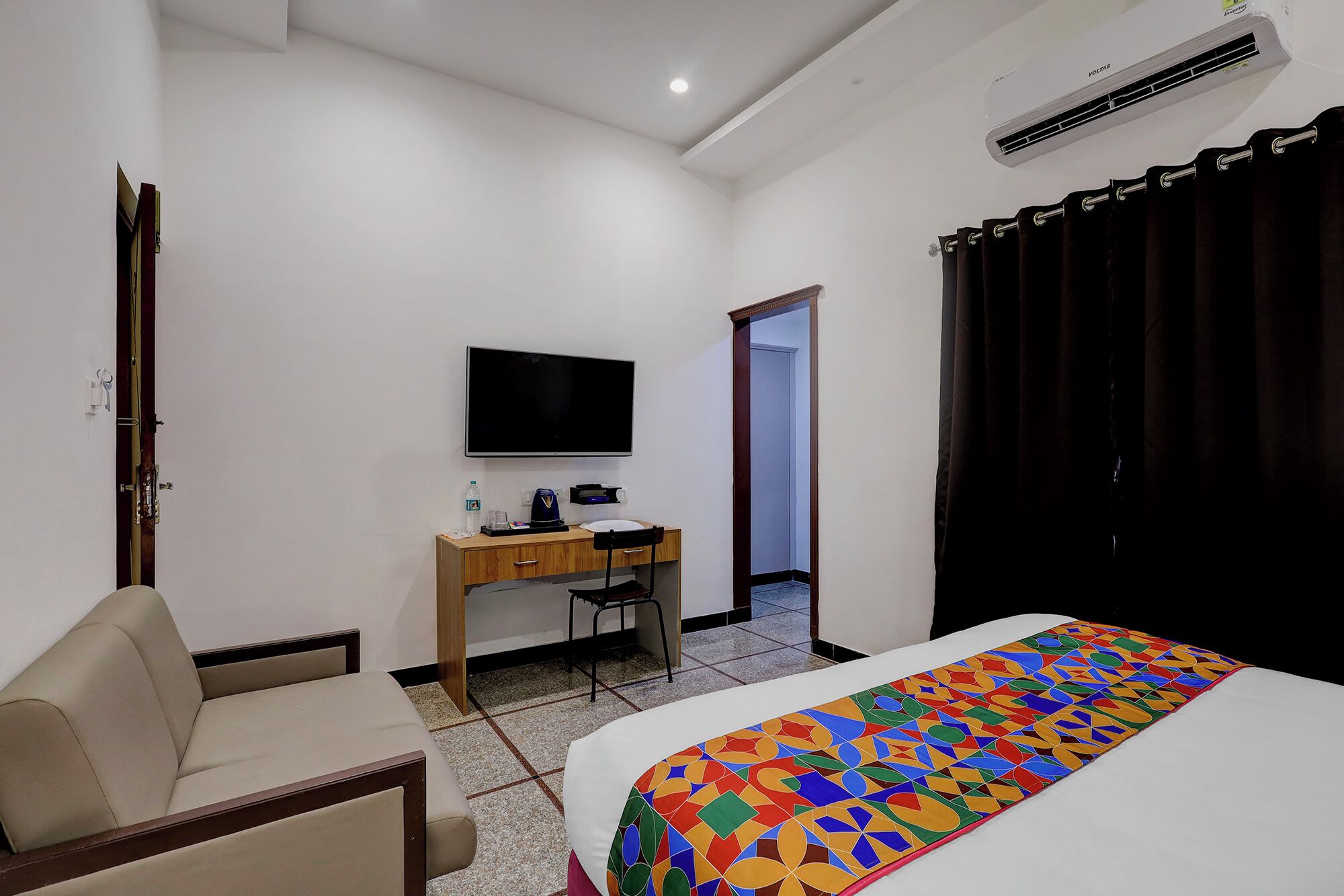 A hotel room with a bed, a desk with a chair, a television, and a bathroom door.