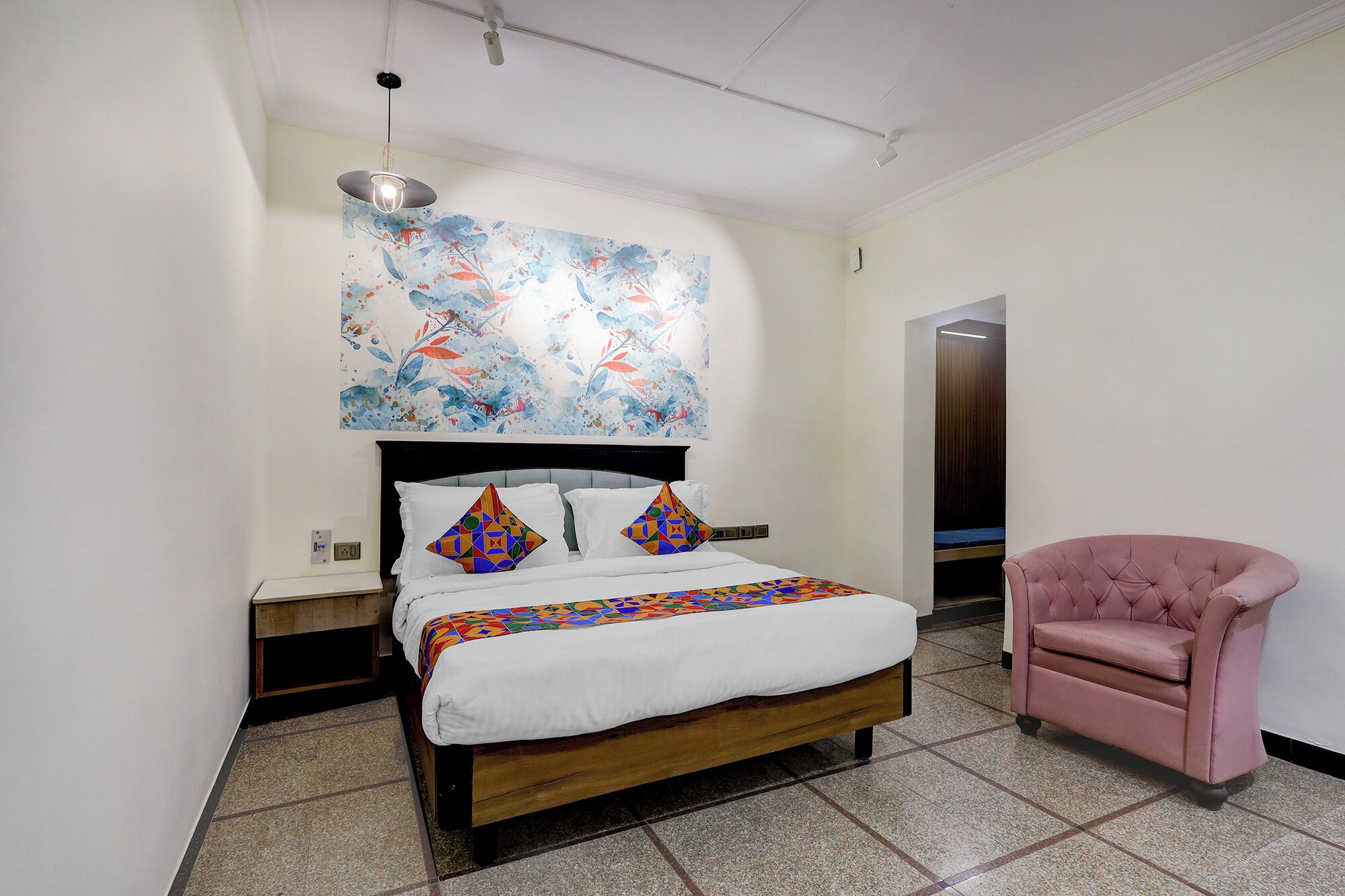 A bedroom with a bed, a pink chair, and a colorful abstract painting on the wall.