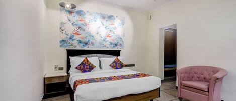 A bedroom with a bed, a pink chair, and a colorful abstract painting on the wall.