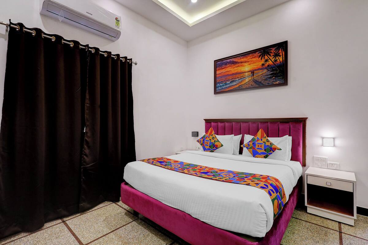 A hotel room with a bed, a painting, a nightstand, and a curtain.
