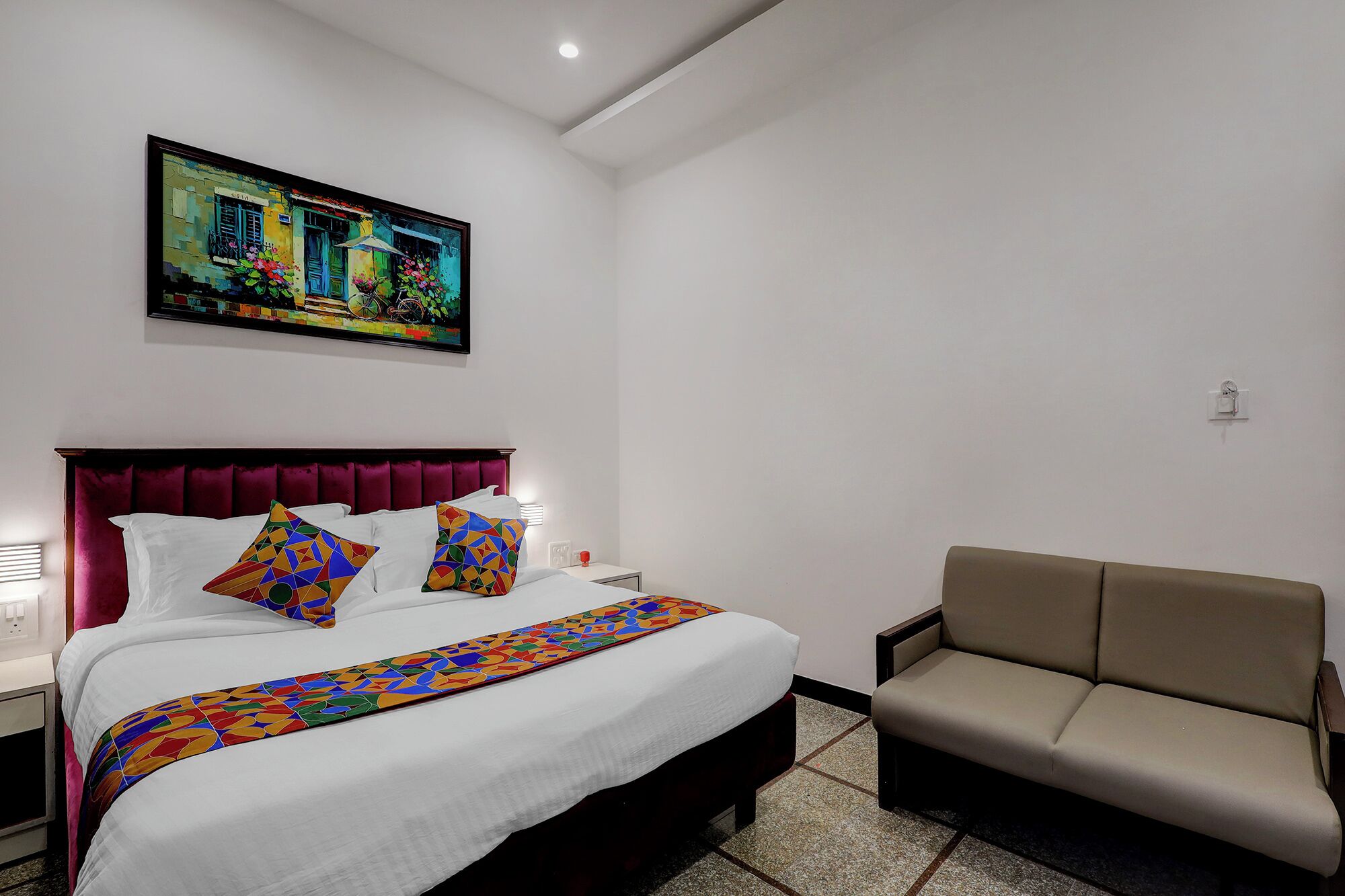 Habitación de hotel con una cama grande, un sofá, un cuadro en la pared y suelo de baldosas.