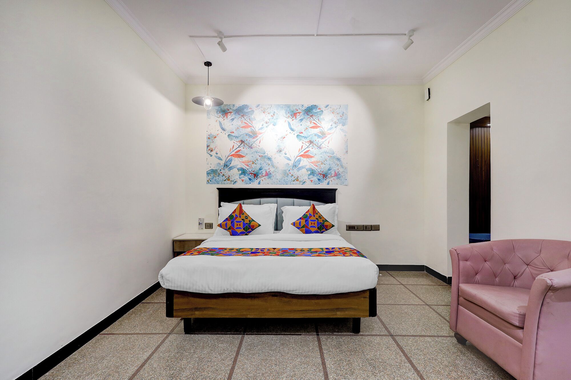 A bedroom with a bed, a pink armchair, a ceiling fan, and a wall-mounted artwork.