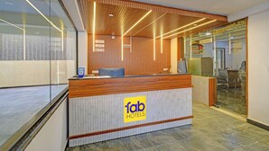 Ein Hotelrezeptionstresen mit Holzausstattung, einer Glastrennwand und einem Schild mit der Aufschrift 'fab hotels'.