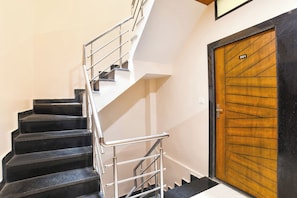 A staircase with metal railings leading to a landing, a wooden door with a number plate, and a white wall. - Fabhotel Div Palace (Indore)