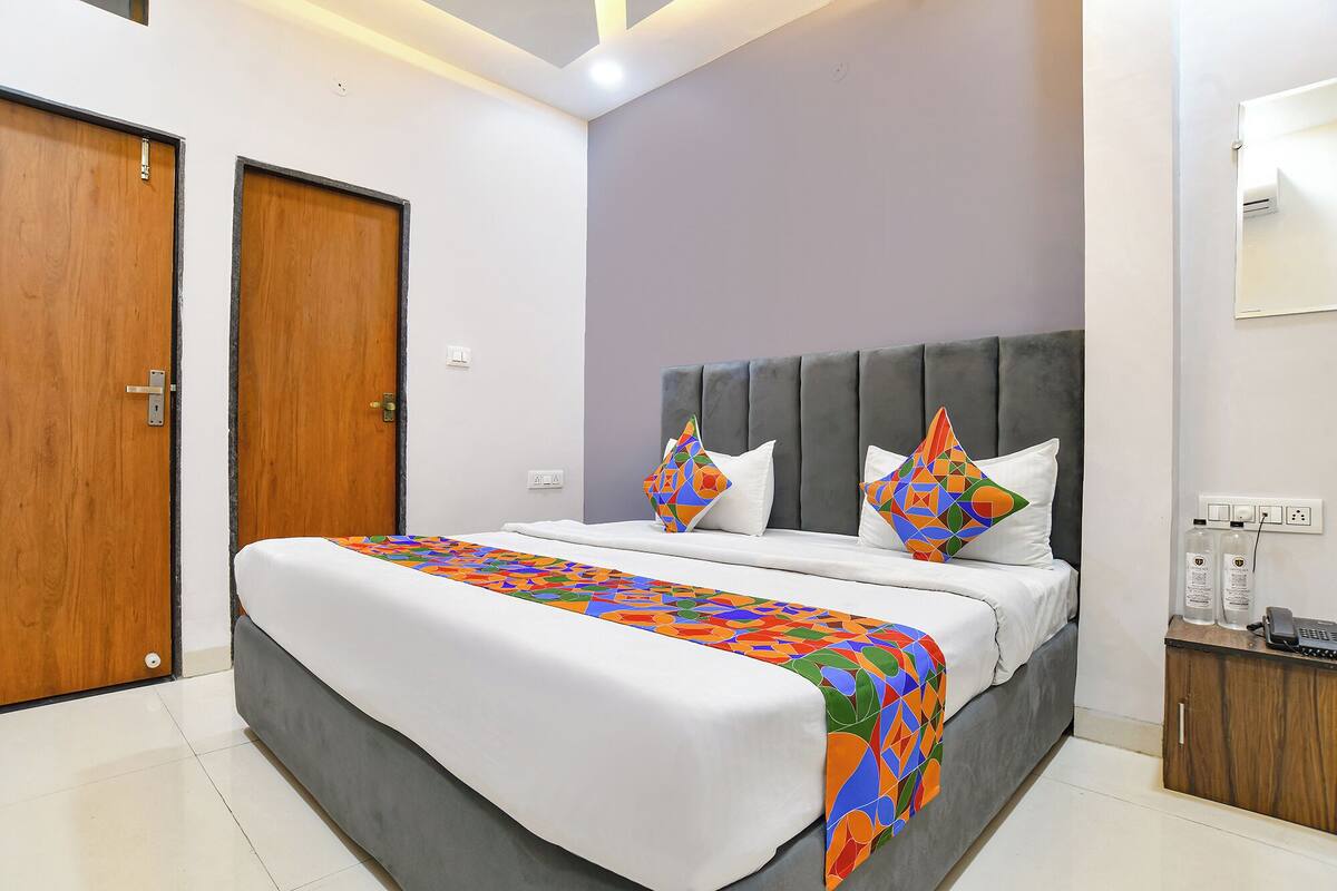 Un dormitorio moderno con un cabecero tapizado en gris, una colcha blanca y almohadas con estampados geométricos coloridos.