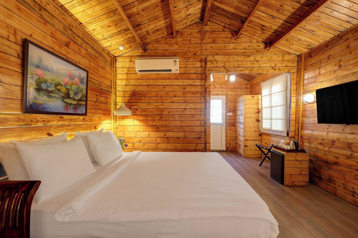Een slaapkamer in een houten blokhut met een bed, een bureau en een schilderij aan de muur.