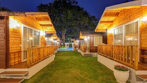 A row of wooden cabins with glass doors and windows, a grassy pathway, and a tree in the center. - FabHotel The Village Boutique Resort - Nr Chapora Fort, Vagator (Vagator)