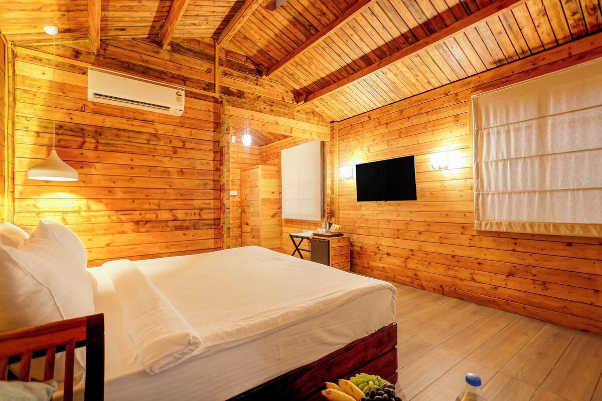 Een houten kamer met een bed, een bureau, een stoel, een televisie en een raam.